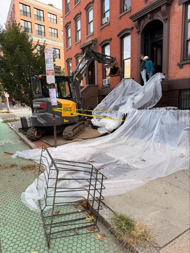 Grove Street, Jersey City: compact excavator working between brownstone staircases
